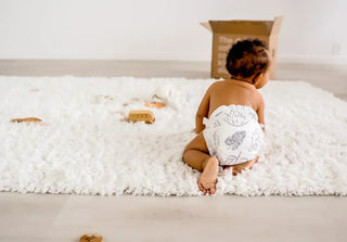 a baby in a diaper crawling on a white shag rug with some toys. 