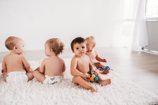 Four babies in diapers sitting on a white rug