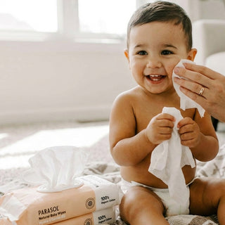Baby holding a tissue with PARASOL Natural Baby Wipes in the foreground
