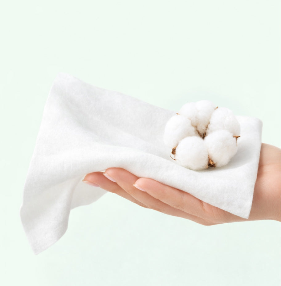 Cotton bolls held in a hand wrapped in a white cloth against a light green background