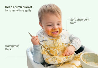 Child wearing a bib with text highlighting features, sitting in a high chair with a bowl.
